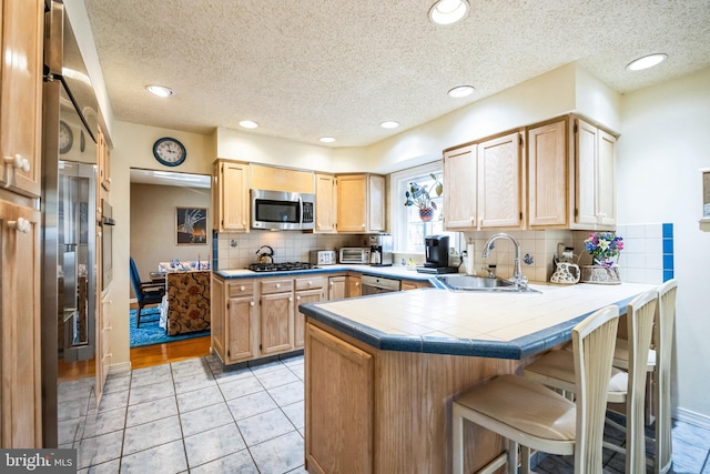 kitchen featuring a breakfast bar area, a peninsula, a sink, appliances with stainless steel finishes, and tasteful backsplash