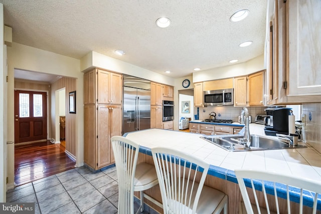 kitchen with stainless steel appliances, a peninsula, a sink, backsplash, and tile counters