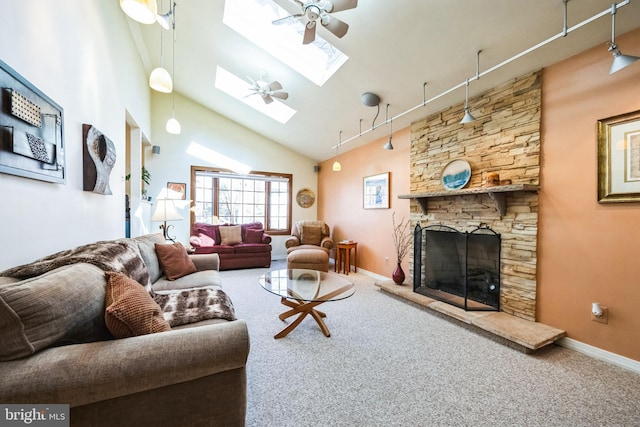 carpeted living room featuring ceiling fan, high vaulted ceiling, a stone fireplace, a skylight, and track lighting