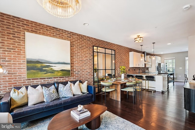 living room with brick wall, dark wood-type flooring, and a notable chandelier