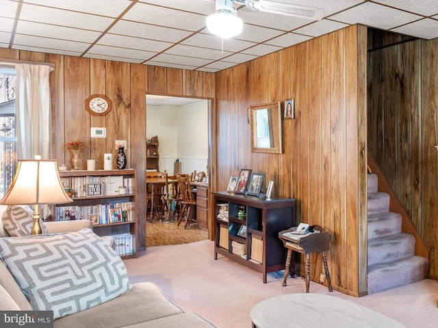 living area featuring wooden walls, light carpet, and a drop ceiling