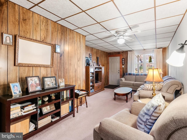 living room featuring a drop ceiling, wooden walls, ceiling fan, and carpet flooring