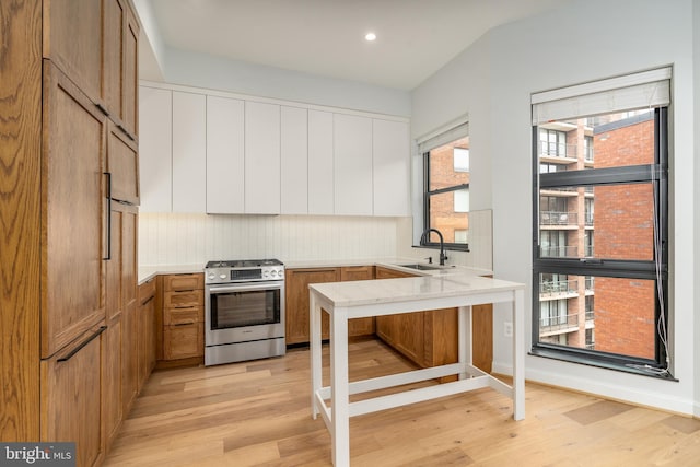 kitchen featuring stainless steel gas stove, sink, tasteful backsplash, and light hardwood / wood-style floors