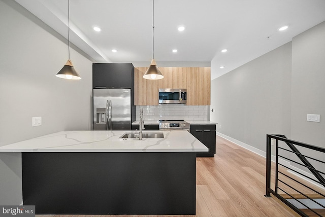 kitchen featuring appliances with stainless steel finishes, decorative light fixtures, sink, light stone countertops, and a center island with sink