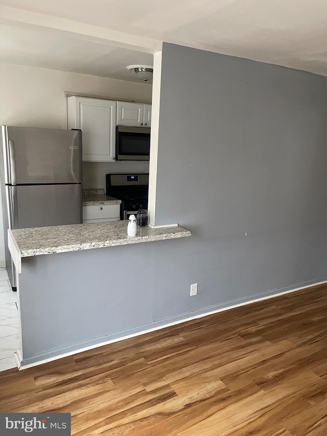 kitchen featuring light hardwood / wood-style flooring, appliances with stainless steel finishes, white cabinetry, light stone countertops, and kitchen peninsula