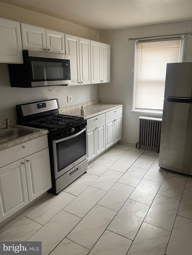 kitchen with white cabinetry, radiator heating unit, and stainless steel appliances