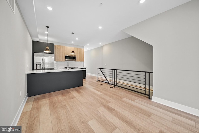 kitchen featuring light hardwood / wood-style flooring, appliances with stainless steel finishes, kitchen peninsula, pendant lighting, and decorative backsplash