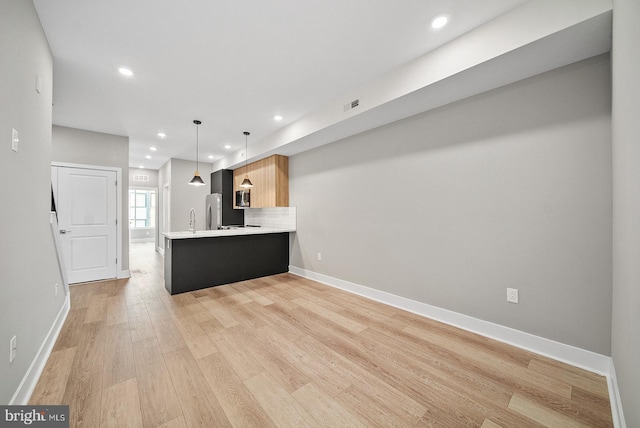 kitchen featuring tasteful backsplash, hanging light fixtures, light hardwood / wood-style flooring, appliances with stainless steel finishes, and kitchen peninsula