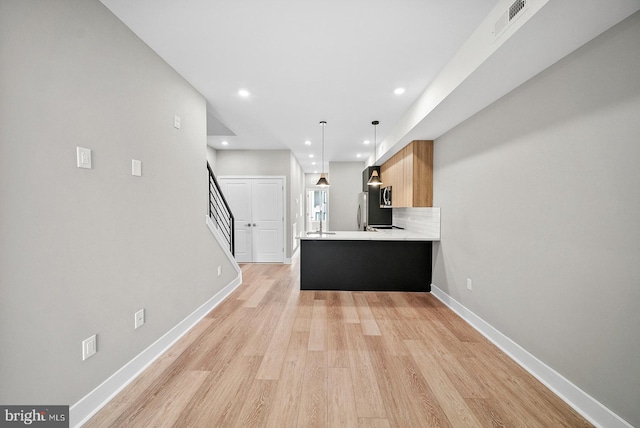 kitchen featuring light hardwood / wood-style flooring, kitchen peninsula, pendant lighting, stainless steel appliances, and decorative backsplash