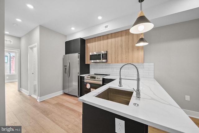 kitchen with hanging light fixtures, light stone countertops, appliances with stainless steel finishes, and kitchen peninsula