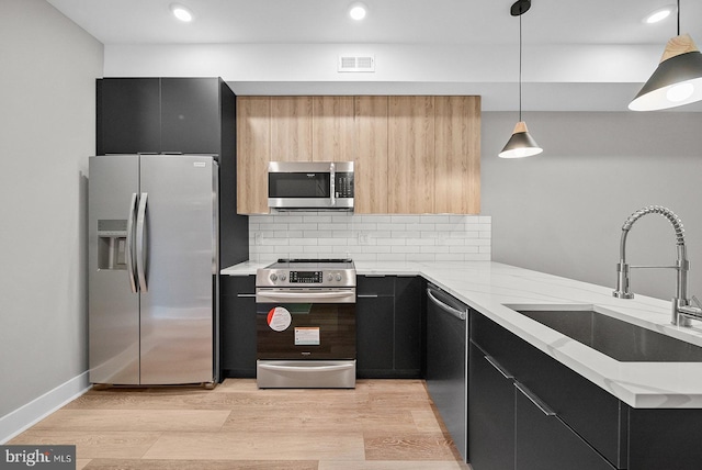 kitchen featuring decorative light fixtures, sink, light hardwood / wood-style floors, kitchen peninsula, and stainless steel appliances