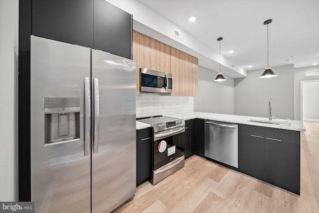 kitchen with sink, hanging light fixtures, kitchen peninsula, stainless steel appliances, and light hardwood / wood-style floors