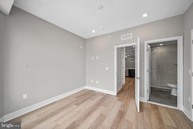 unfurnished bedroom with ensuite bath and light wood-type flooring