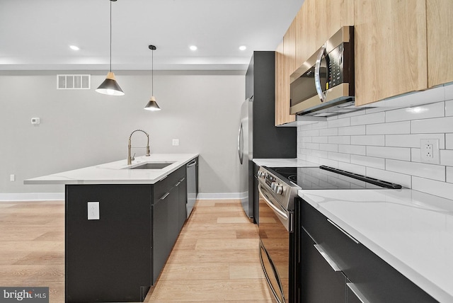 kitchen with sink, decorative light fixtures, appliances with stainless steel finishes, light stone countertops, and light hardwood / wood-style floors