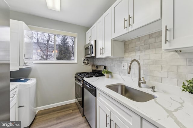 kitchen featuring sink, washer and dryer, light stone counters, appliances with stainless steel finishes, and white cabinets