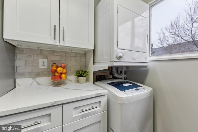 clothes washing area with stacked washer / dryer and cabinets