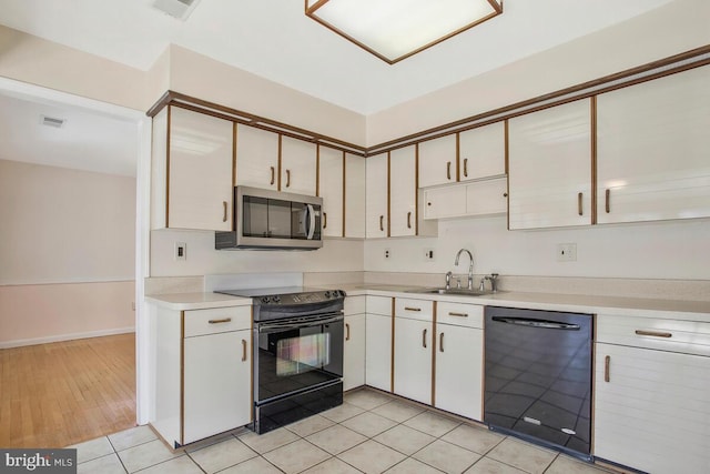 kitchen featuring white cabinetry, sink, light tile patterned floors, and black appliances