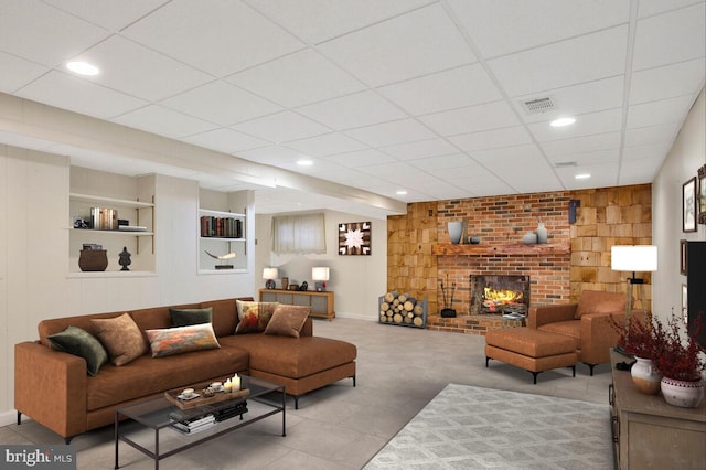 living room with a brick fireplace, a paneled ceiling, wood walls, and built in shelves