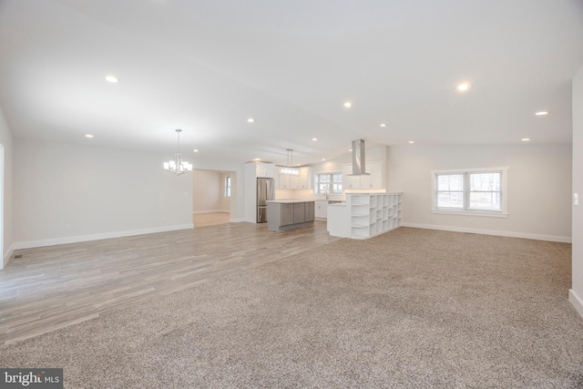 unfurnished living room with lofted ceiling, an inviting chandelier, baseboards, and light colored carpet