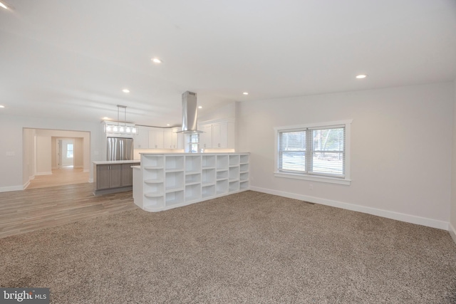 unfurnished living room featuring recessed lighting, baseboards, a notable chandelier, and light colored carpet