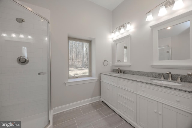 bathroom featuring tiled shower, a sink, baseboards, and double vanity