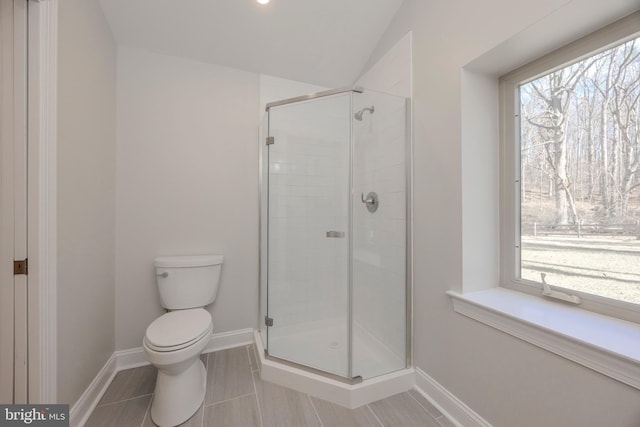 bathroom with a stall shower, plenty of natural light, toilet, and baseboards