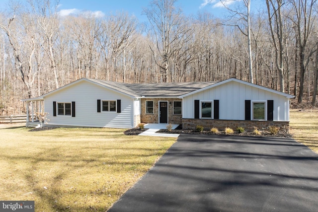 view of front of home with board and batten siding, stone siding, fence, and a front lawn