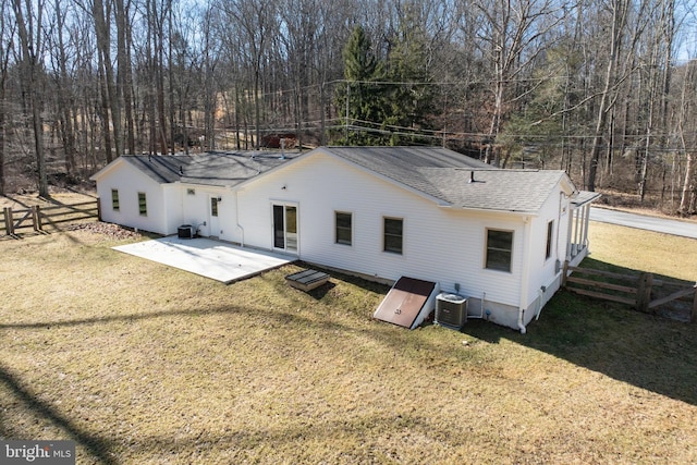 rear view of house with central AC, a lawn, fence, and roof with shingles