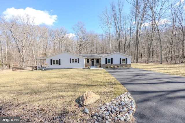 ranch-style home with driveway, a view of trees, stone siding, fence, and a front lawn