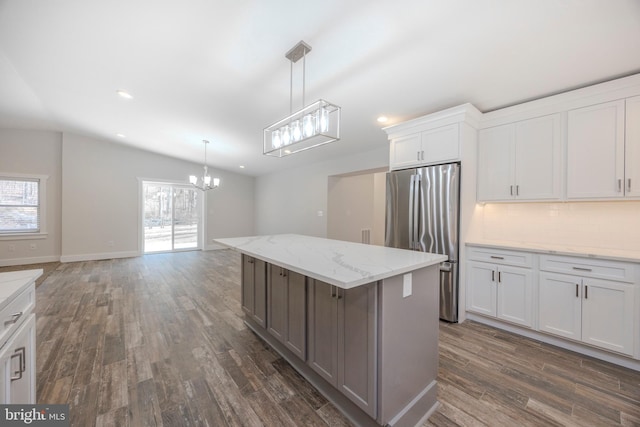 kitchen with dark wood-type flooring, white cabinets, freestanding refrigerator, a center island, and decorative light fixtures