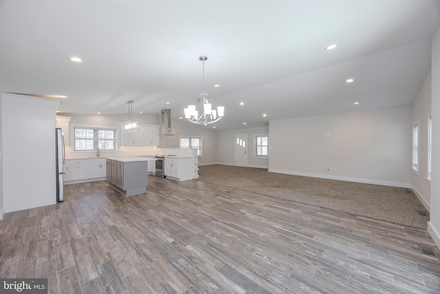 kitchen featuring stainless steel appliances, a kitchen island, open floor plan, vaulted ceiling, and wall chimney range hood