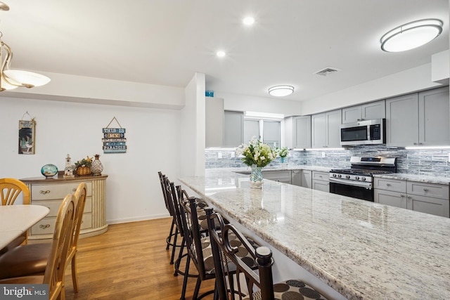 kitchen featuring light stone counters, a kitchen breakfast bar, appliances with stainless steel finishes, gray cabinets, and decorative backsplash