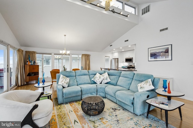 living area featuring high vaulted ceiling, visible vents, a notable chandelier, and light wood-style flooring