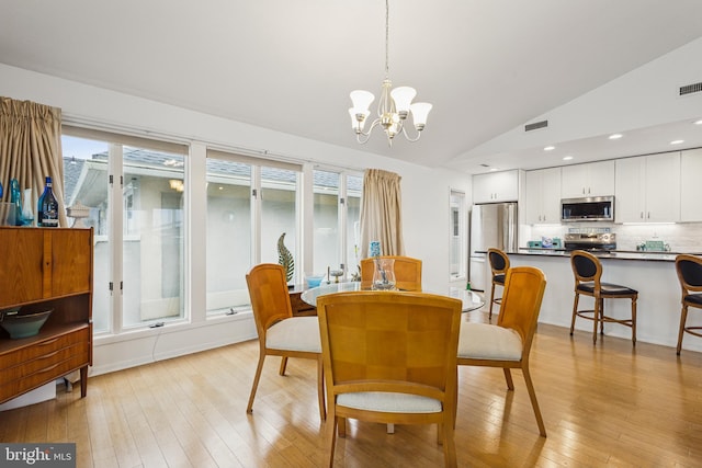 dining space featuring lofted ceiling, light wood-type flooring, visible vents, and a notable chandelier