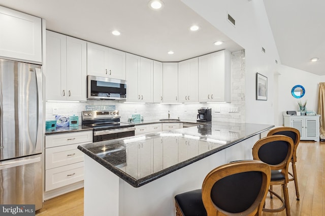 kitchen with light wood-type flooring, a breakfast bar area, stainless steel appliances, and dark stone countertops