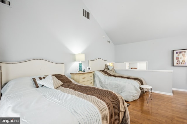 bedroom with high vaulted ceiling, visible vents, baseboards, and wood finished floors