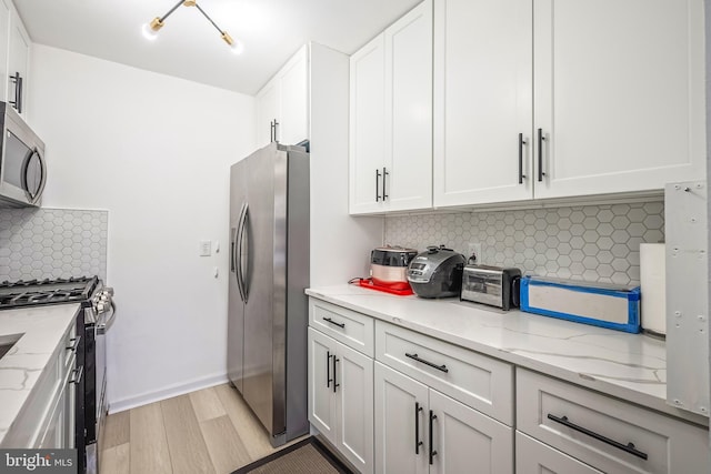 kitchen featuring white cabinetry, appliances with stainless steel finishes, light stone countertops, light hardwood / wood-style floors, and decorative backsplash