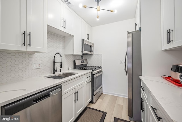 kitchen featuring sink, white cabinetry, light stone counters, light wood-type flooring, and stainless steel appliances