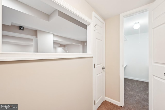 hallway featuring dark carpet and baseboards