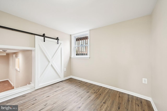 spare room featuring a barn door, wood finished floors, and baseboards