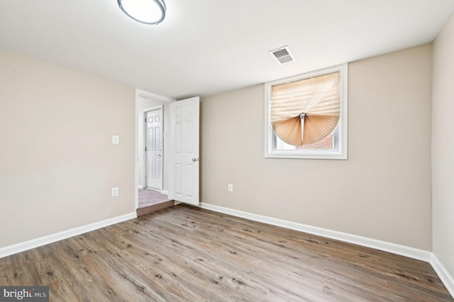 empty room featuring wood finished floors, visible vents, and baseboards