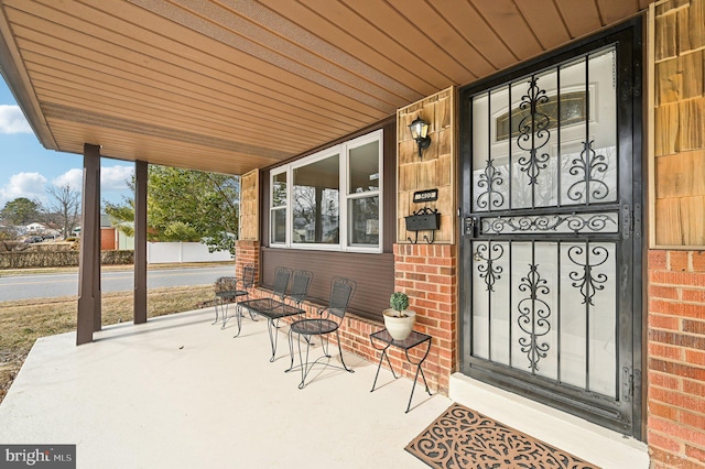 doorway to property featuring a porch and brick siding