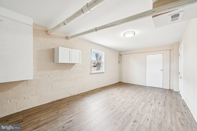 empty room with concrete block wall, visible vents, and light wood-style floors