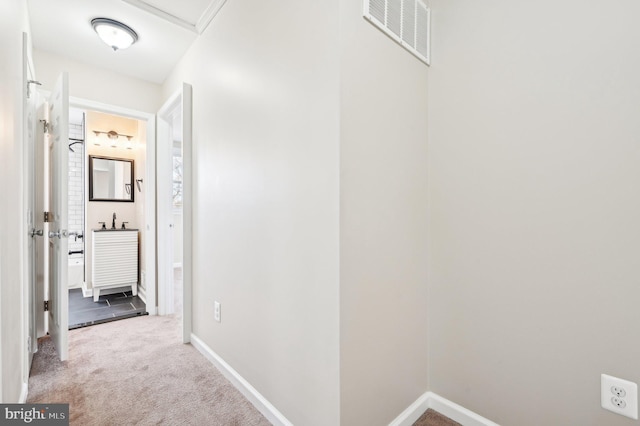 hallway with carpet, visible vents, a sink, and baseboards