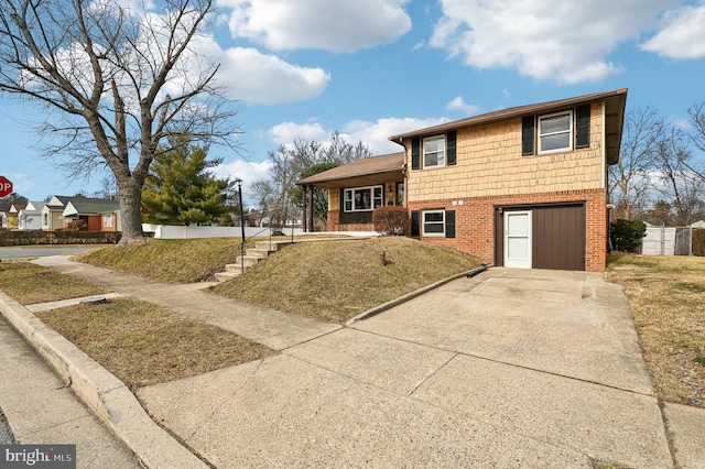 tri-level home with concrete driveway, brick siding, stairway, and a front lawn