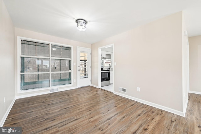 unfurnished room with wood finished floors, visible vents, and baseboards