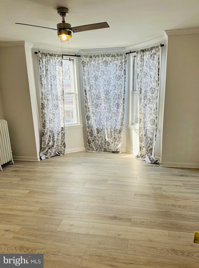 empty room featuring crown molding, radiator heating unit, ceiling fan, and light wood-type flooring