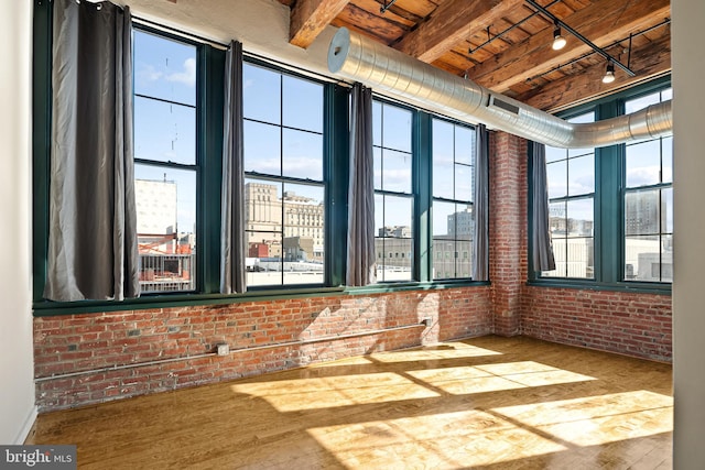 interior space with brick wall, wood finished floors, rail lighting, a view of city, and beam ceiling