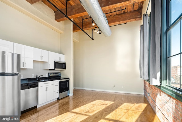 kitchen with stainless steel appliances, dark countertops, a high ceiling, white cabinets, and a sink