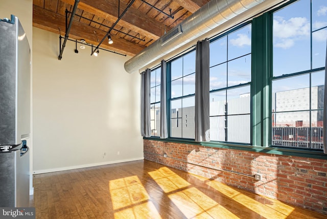 empty room featuring a city view, rail lighting, wood ceiling, wood finished floors, and baseboards